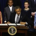 Obama signing laws in front of a bunch of kids